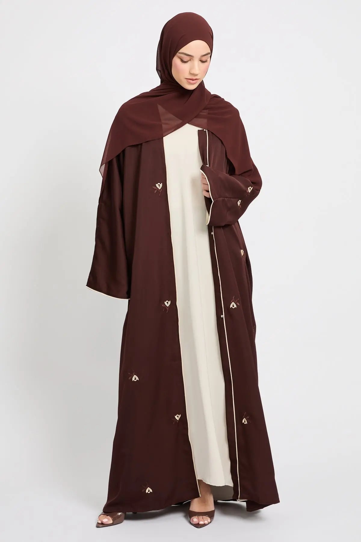 Woman wearing a brown abaya with white accents on a white background