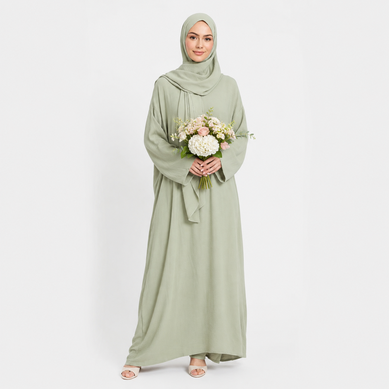 Woman wearing a light green hijab and dress holding flowers on a white background