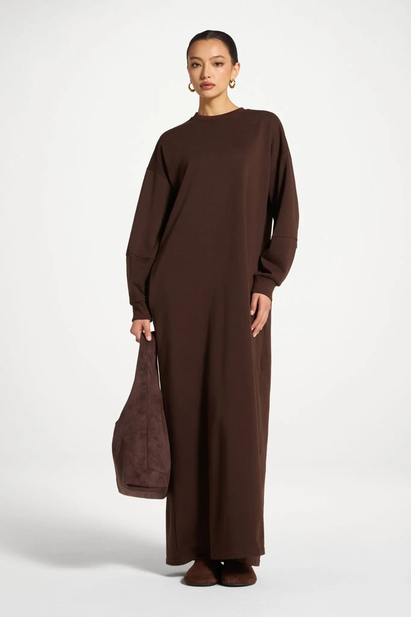 Woman wearing a brown long-sleeve dress holding a matching bag on a white background