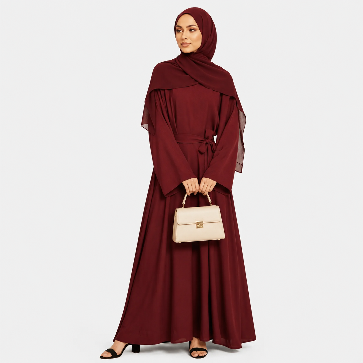 Woman wearing a burgundy abaya holding a beige handbag on a white background