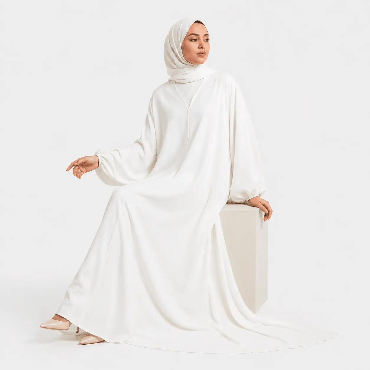 Woman wearing a white abaya and hijab on a white background
