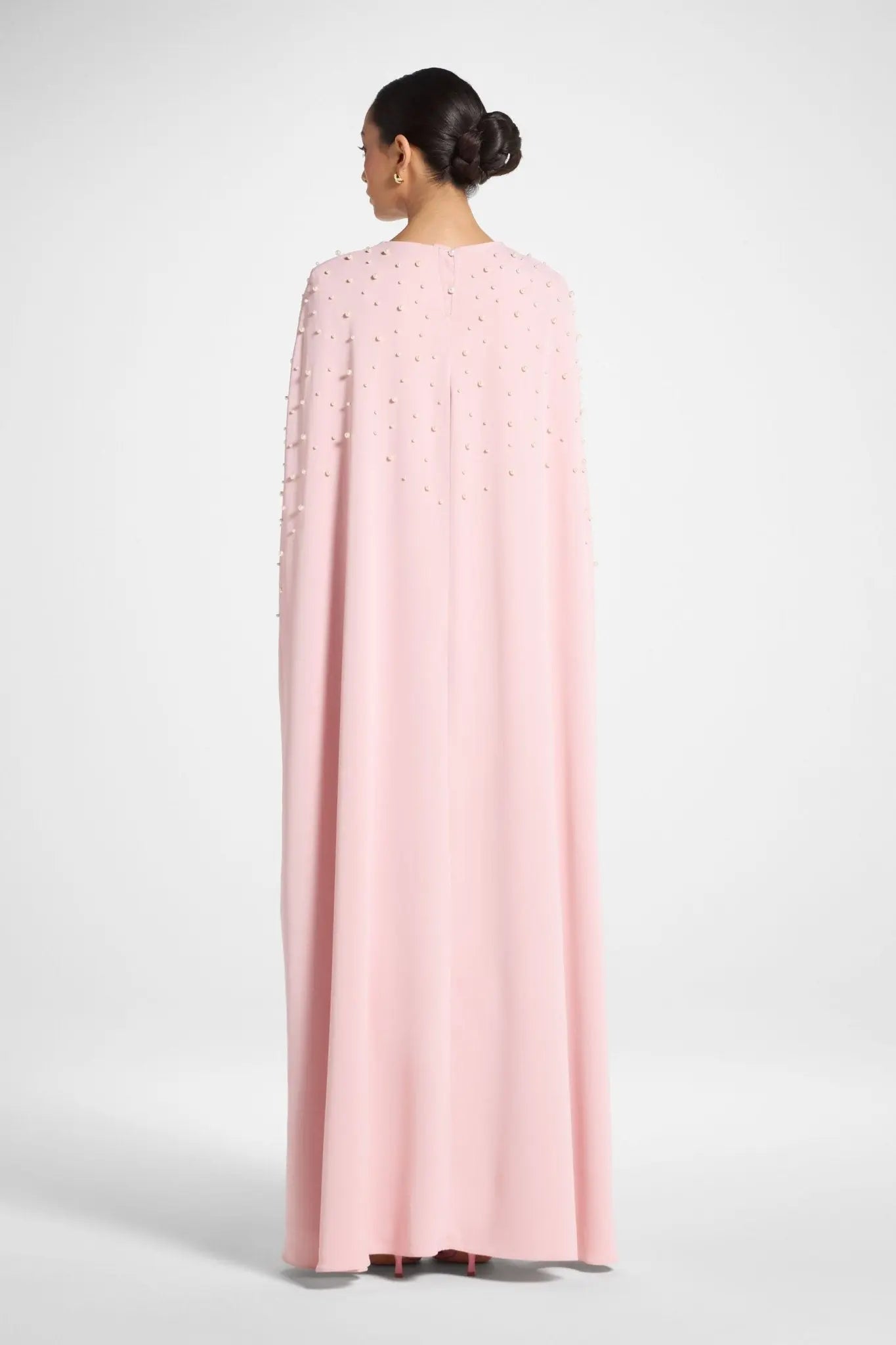 Person wearing a pink cape with white embellishments on a white background