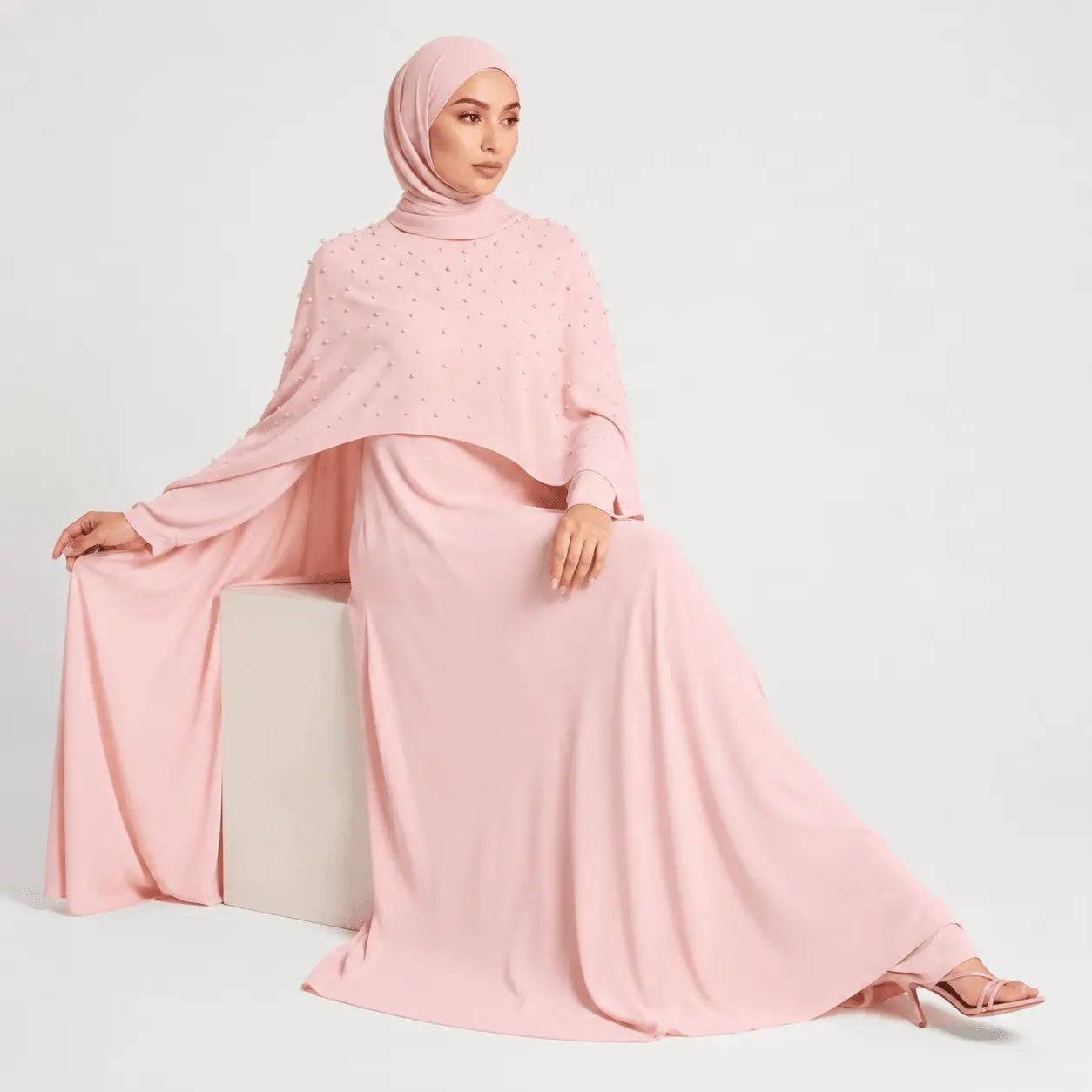 Woman wearing a pink outfit with a matching hijab on a white background