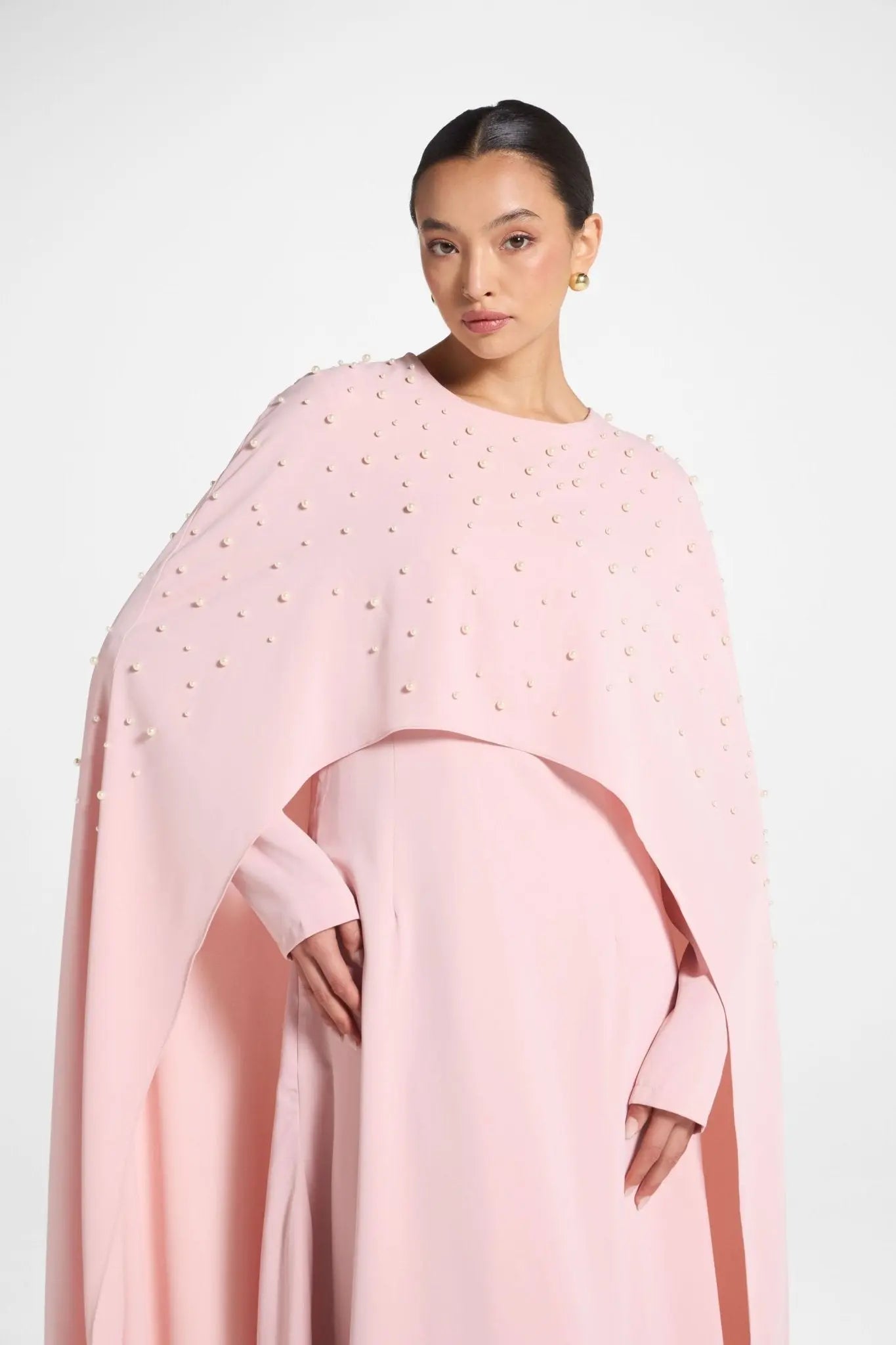 Woman wearing a pink cape with embellishments on a white background