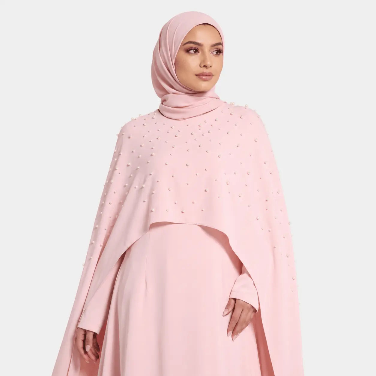 Woman wearing a pink outfit with a matching hijab on a light gray background