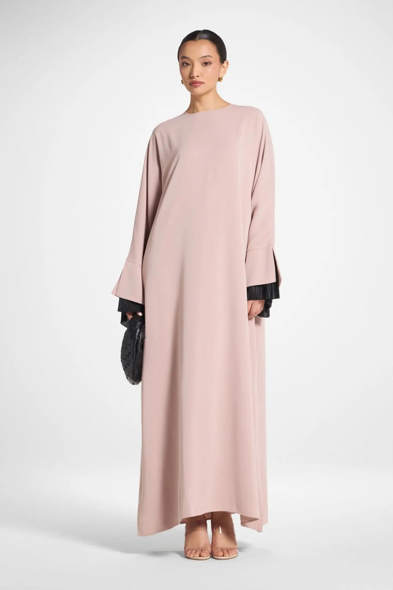 Woman wearing a long light pink dress with black cuffs on a white background