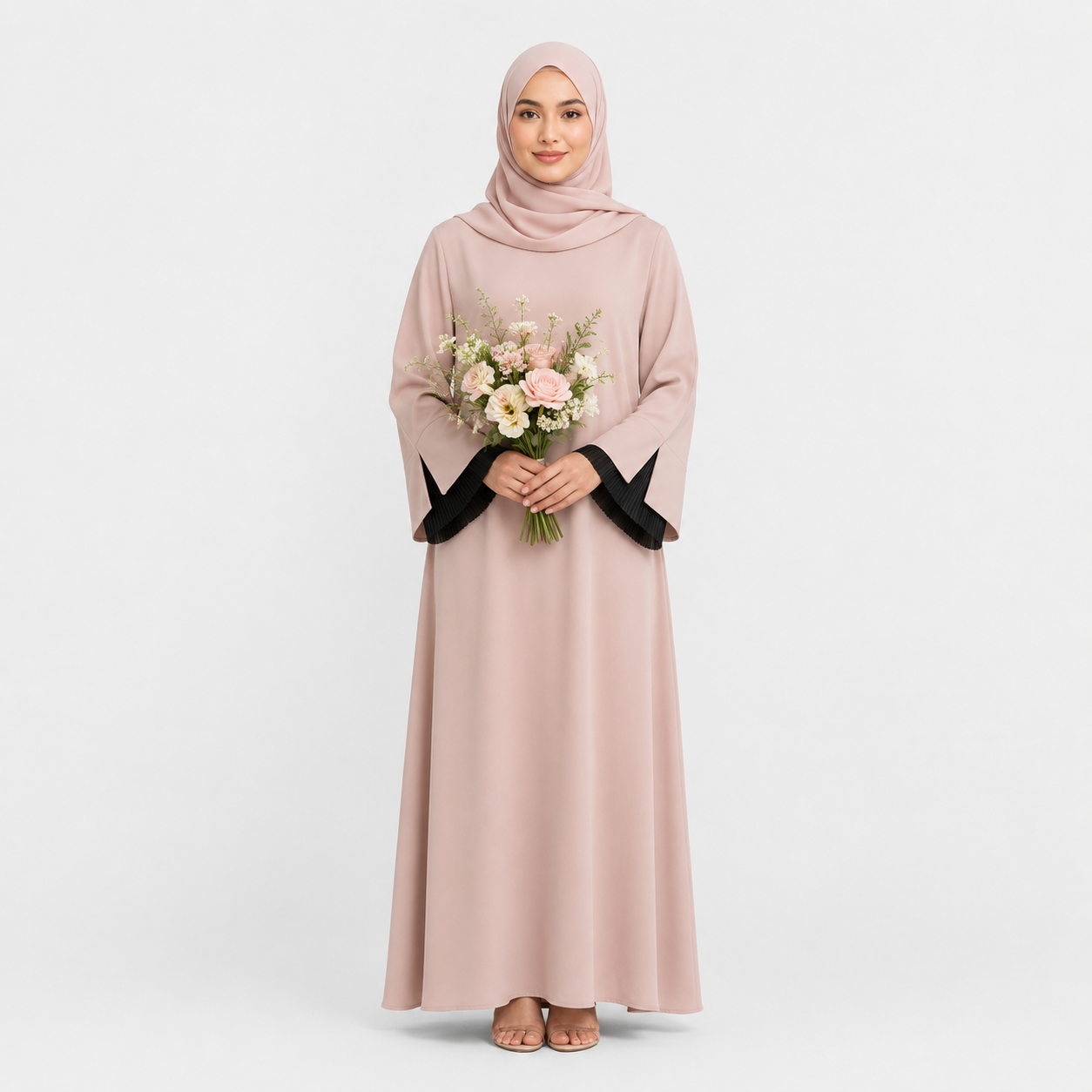 Woman wearing a long light pink dress with black cuffs and holding flowers on a white background