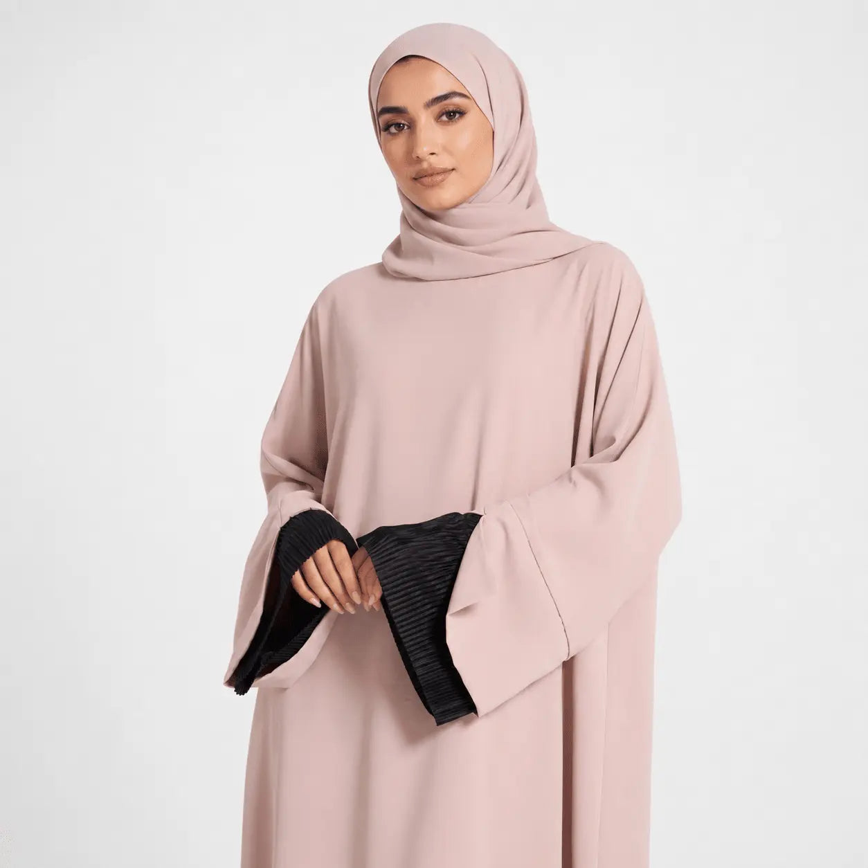 Woman wearing a light pink abaya with black cuffs on a white background