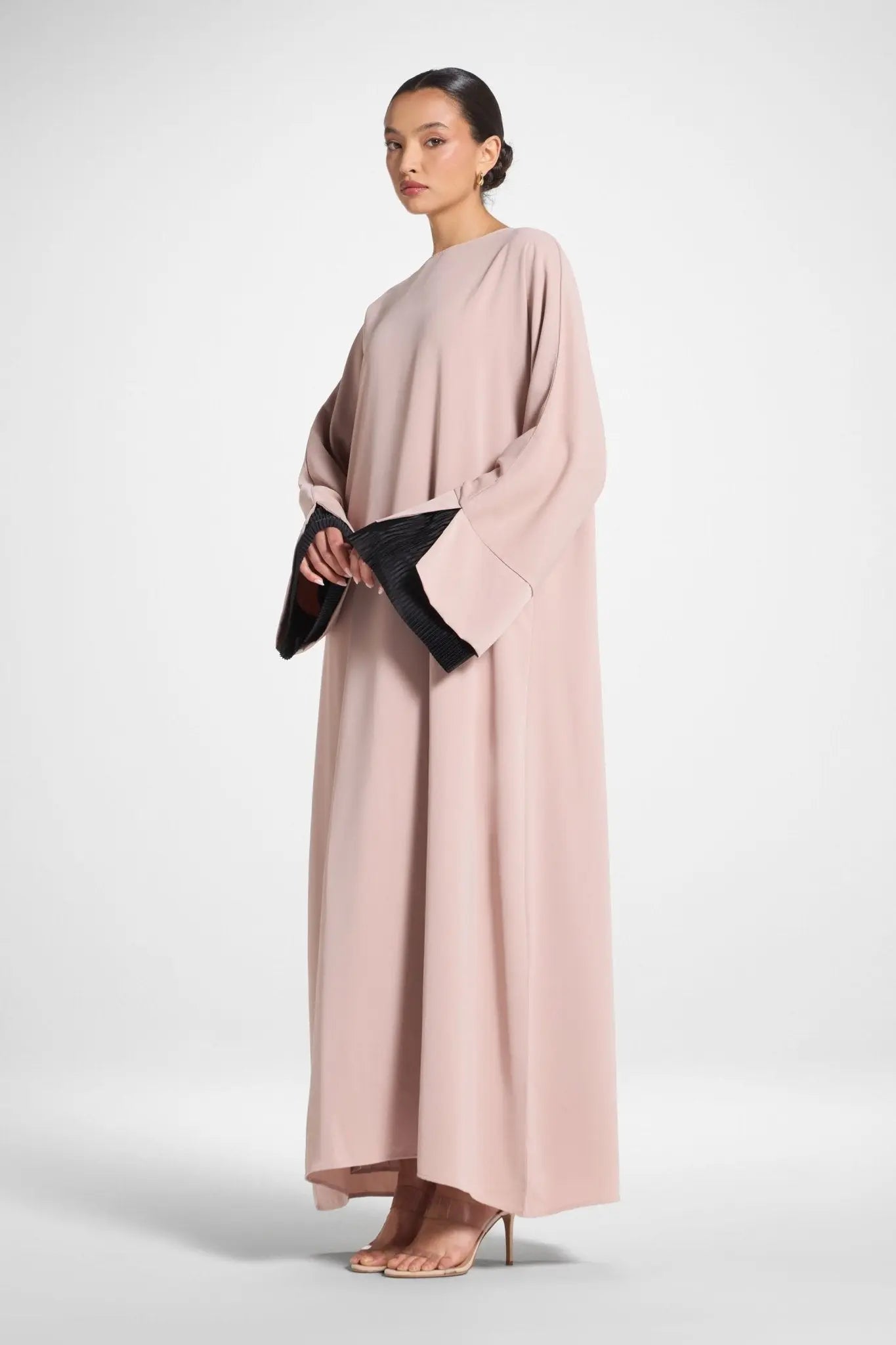 Woman wearing a long, light pink dress with black gloves on a white background