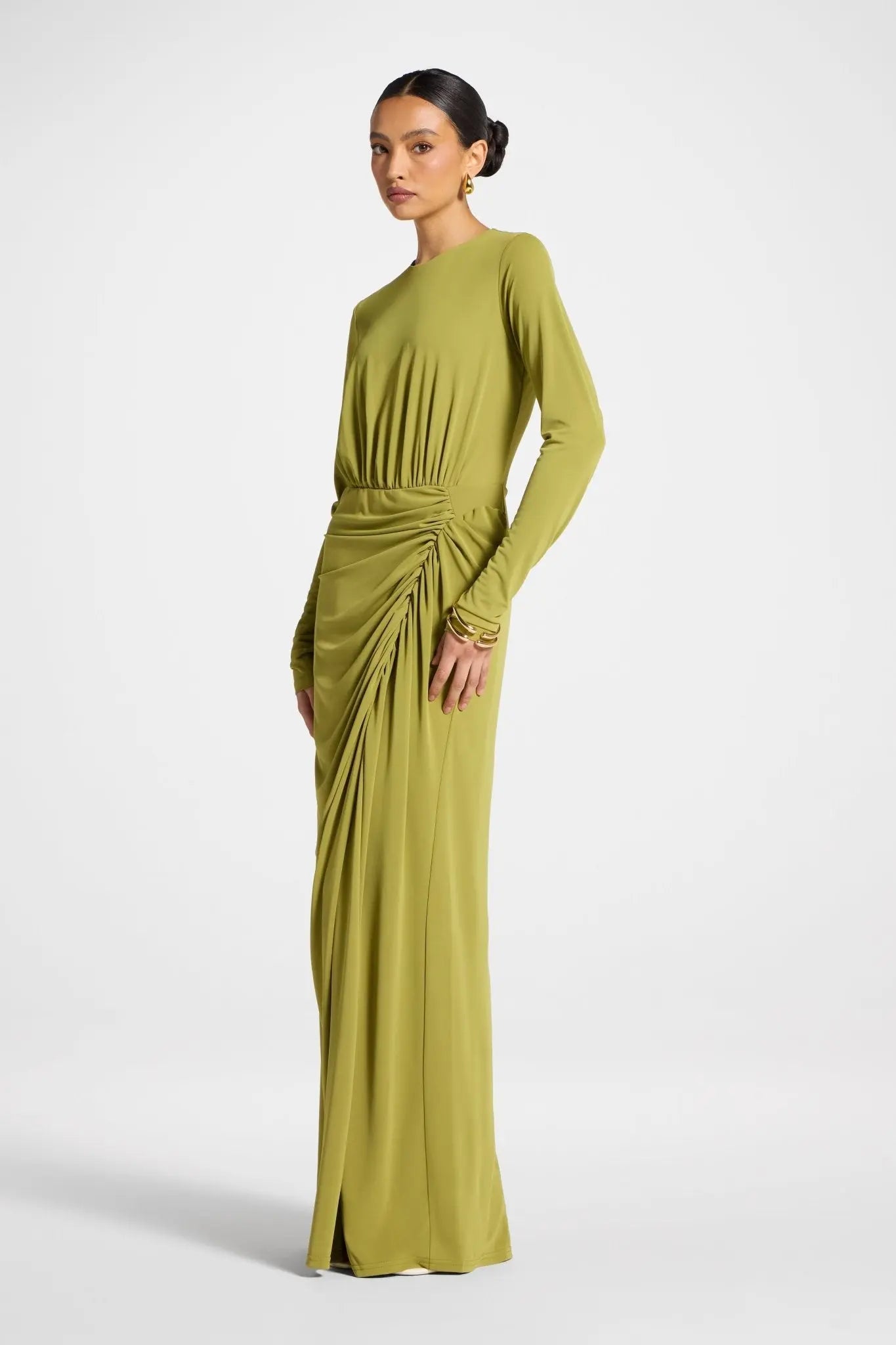 Woman wearing a long green dress with a gathered waist on a white background
