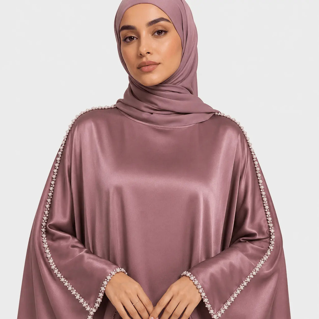 Woman wearing a mauve hijab with embellished edges on a light gray background