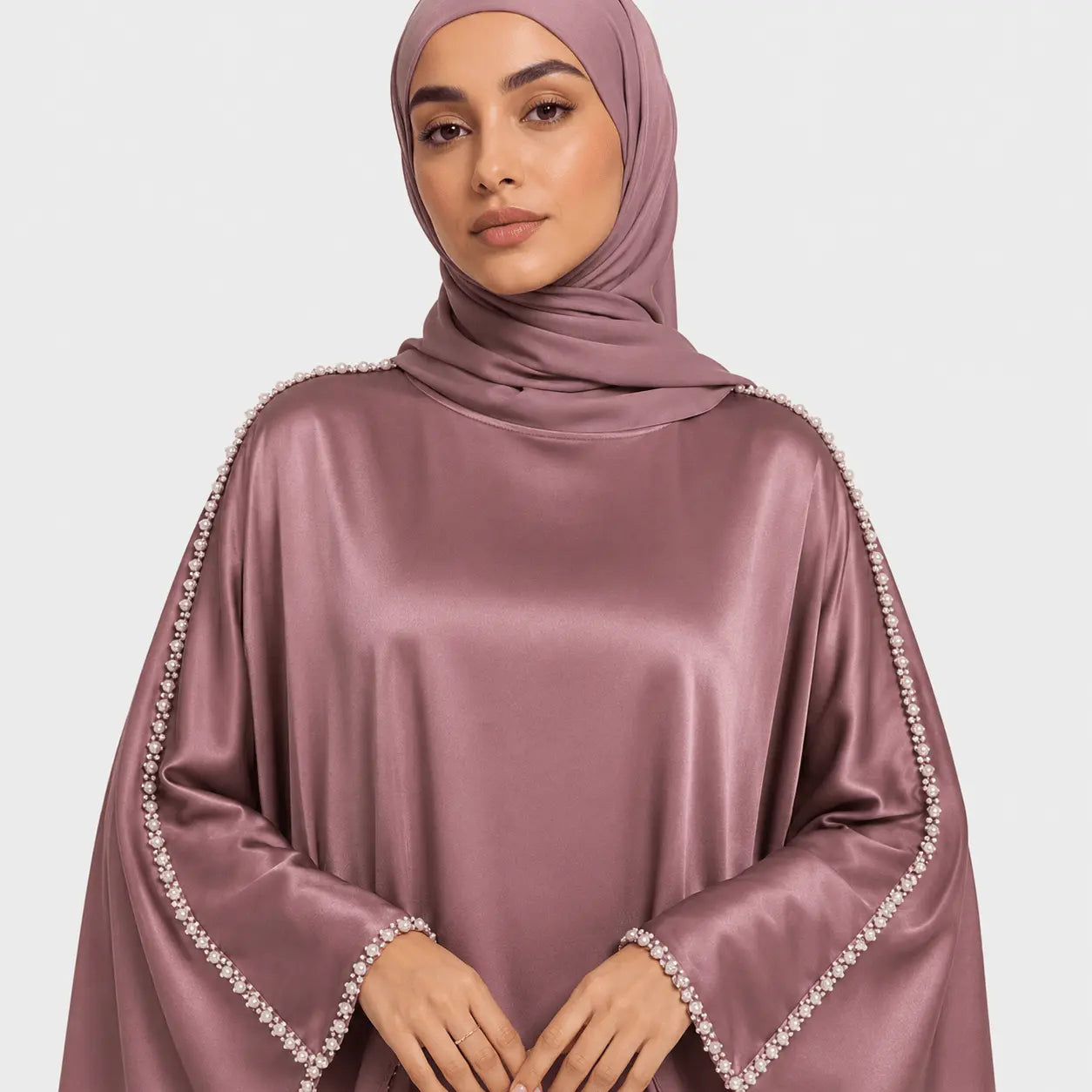 Woman wearing a mauve hijab with embellished edges on a light gray background