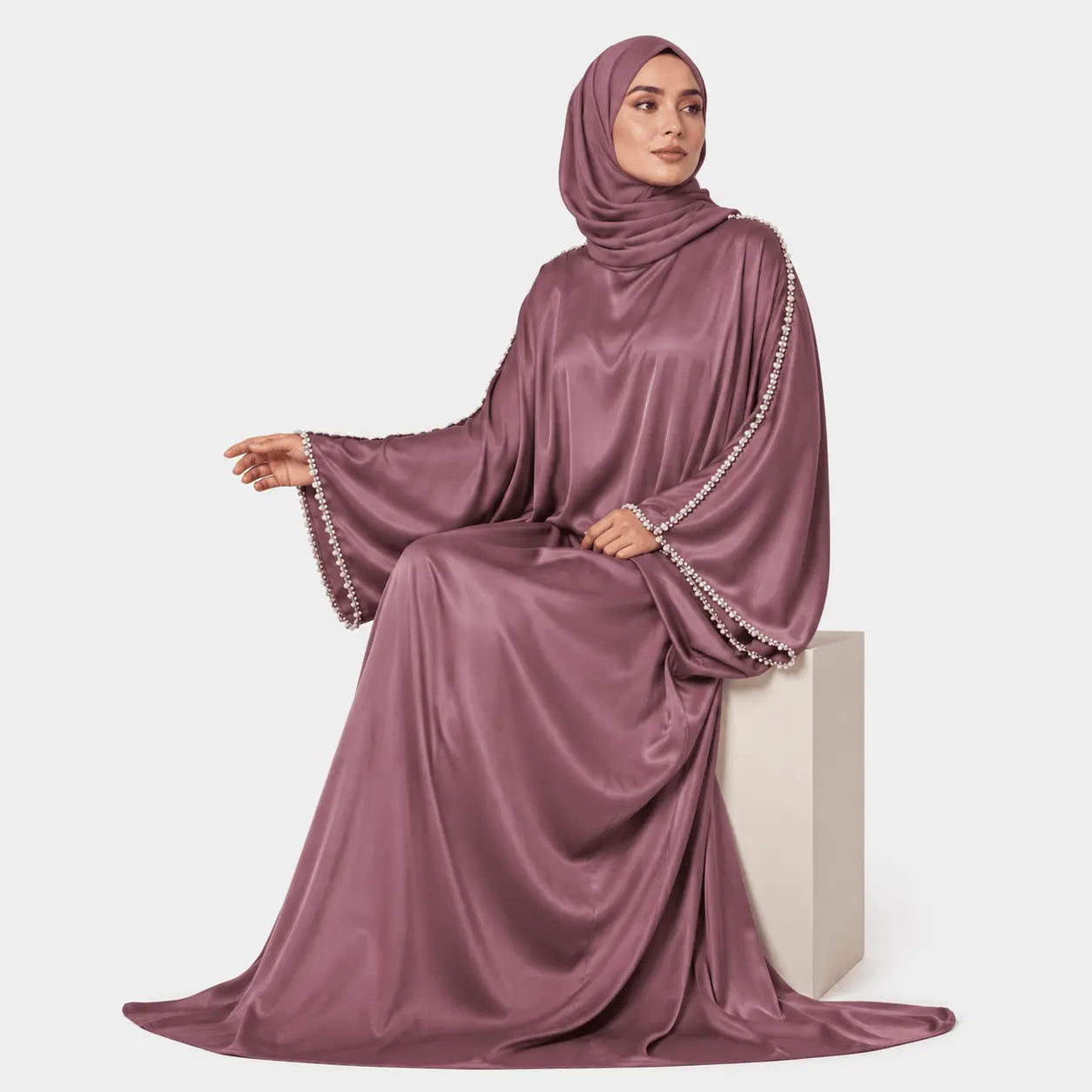 Woman wearing a mauve abaya with intricate detailing on a white background