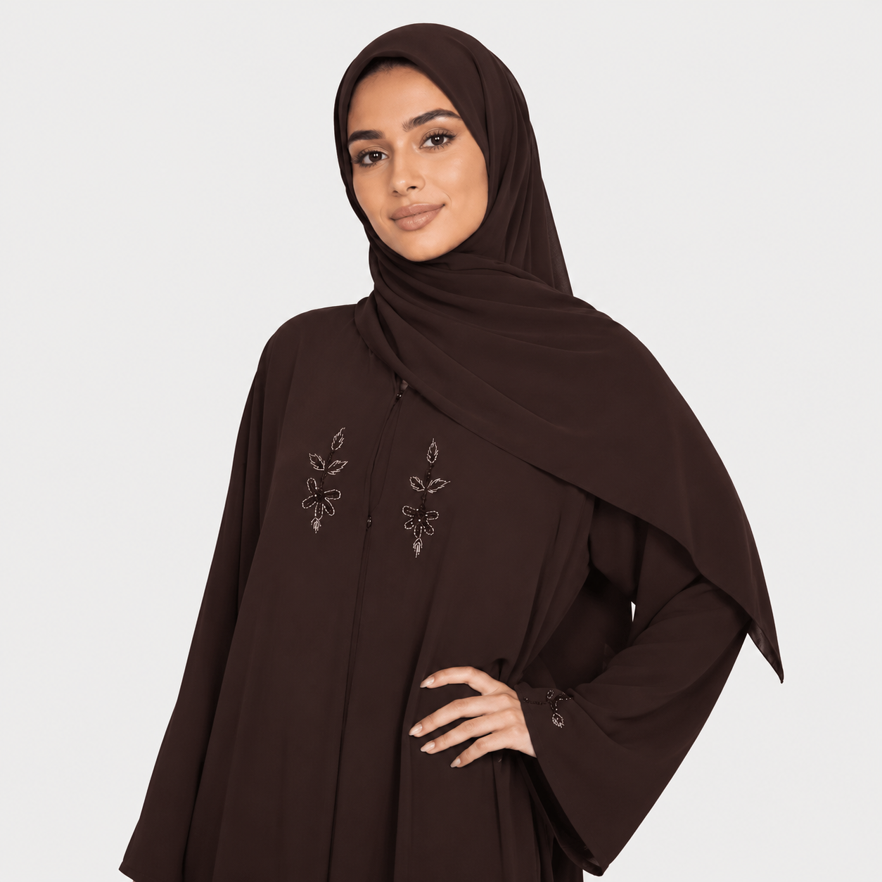Woman wearing a brown abaya with floral embroidery on a white background