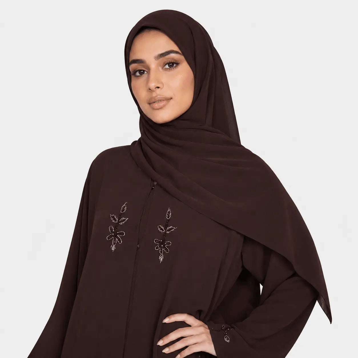 Woman wearing a brown hijab with intricate designs on a white background