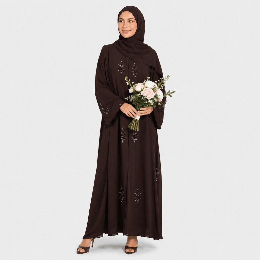 Woman wearing a dark brown dress with floral embroidery, holding a bouquet of flowers on a white background