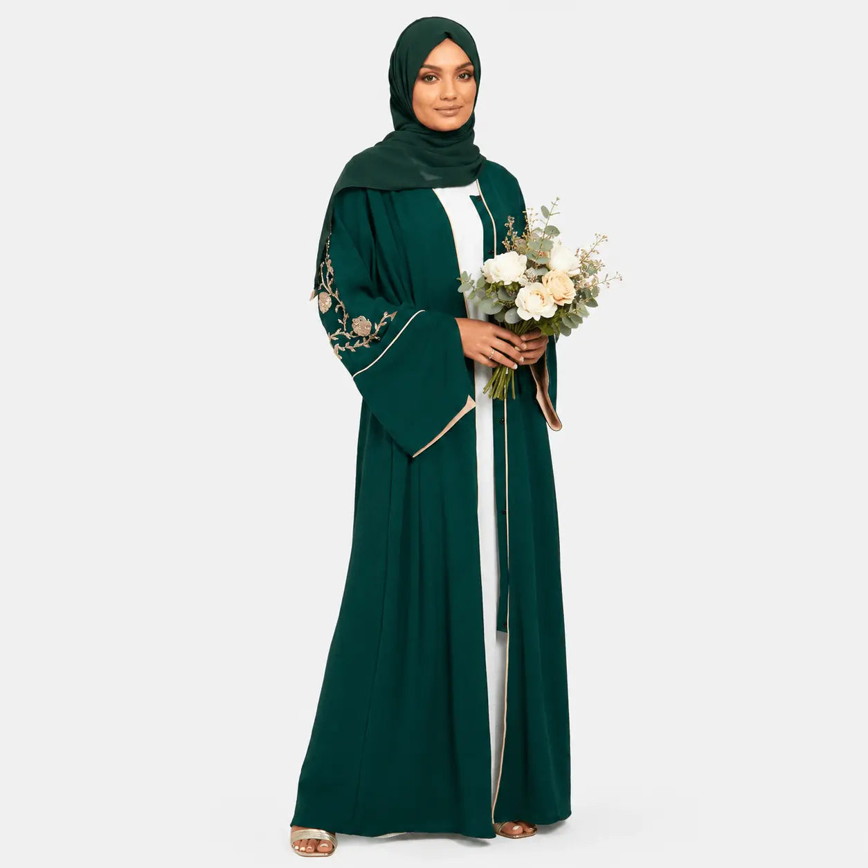 Woman wearing a green abaya with floral embroidery, holding flowers on a white background