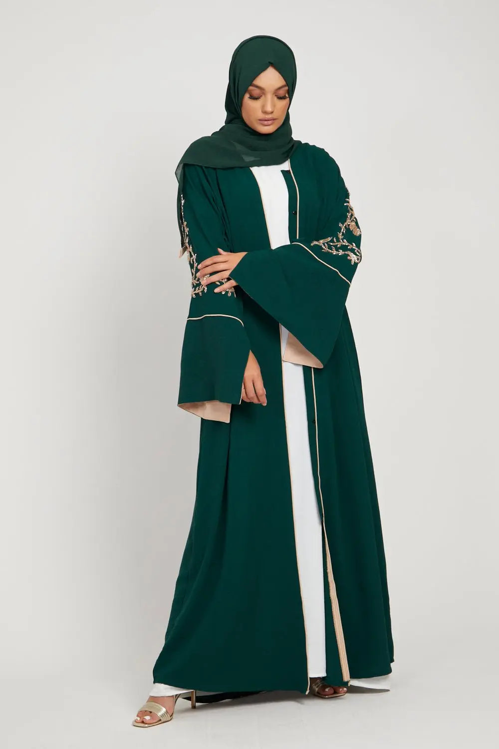 Woman wearing a green abaya with white accents on a white background