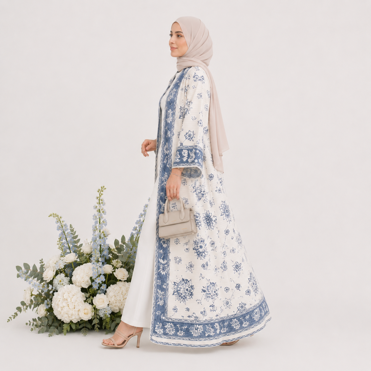 Woman in a floral dress with a hijab standing next to a floral arrangement on a white background
