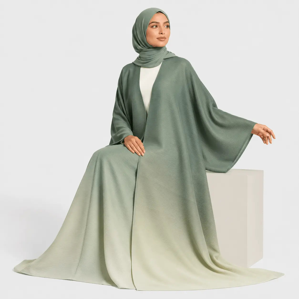 Woman wearing a long, light green abaya with a matching hijab on a white background