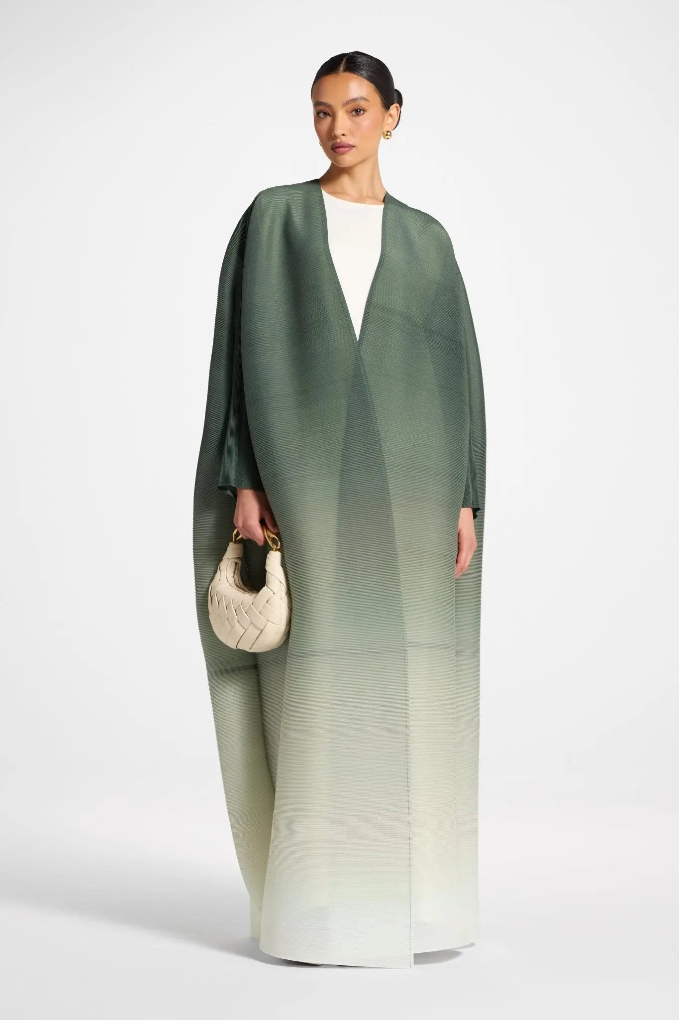 Woman wearing a green and white gradient dress holding a beige handbag on a white background