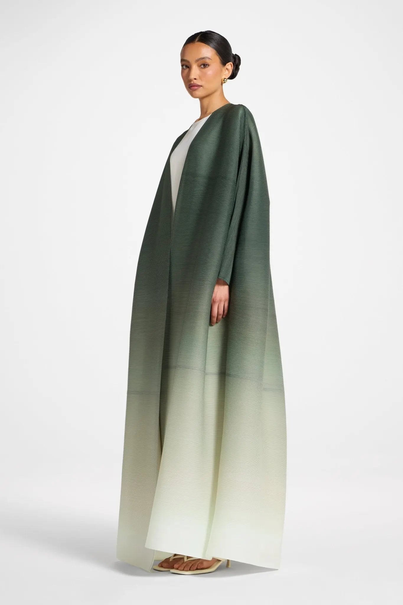 Woman wearing a long, green to white gradient dress on a white background