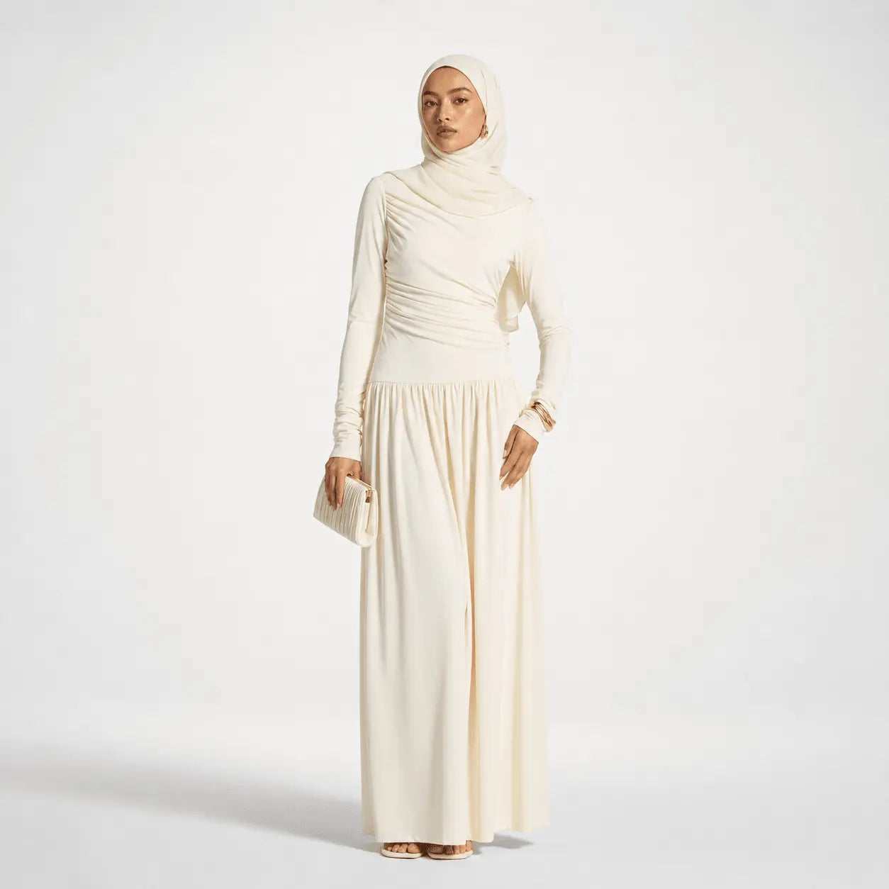 Cream hijab dress with ruched bodice, long sleeves, and flowing skirt, paired with matching clutch