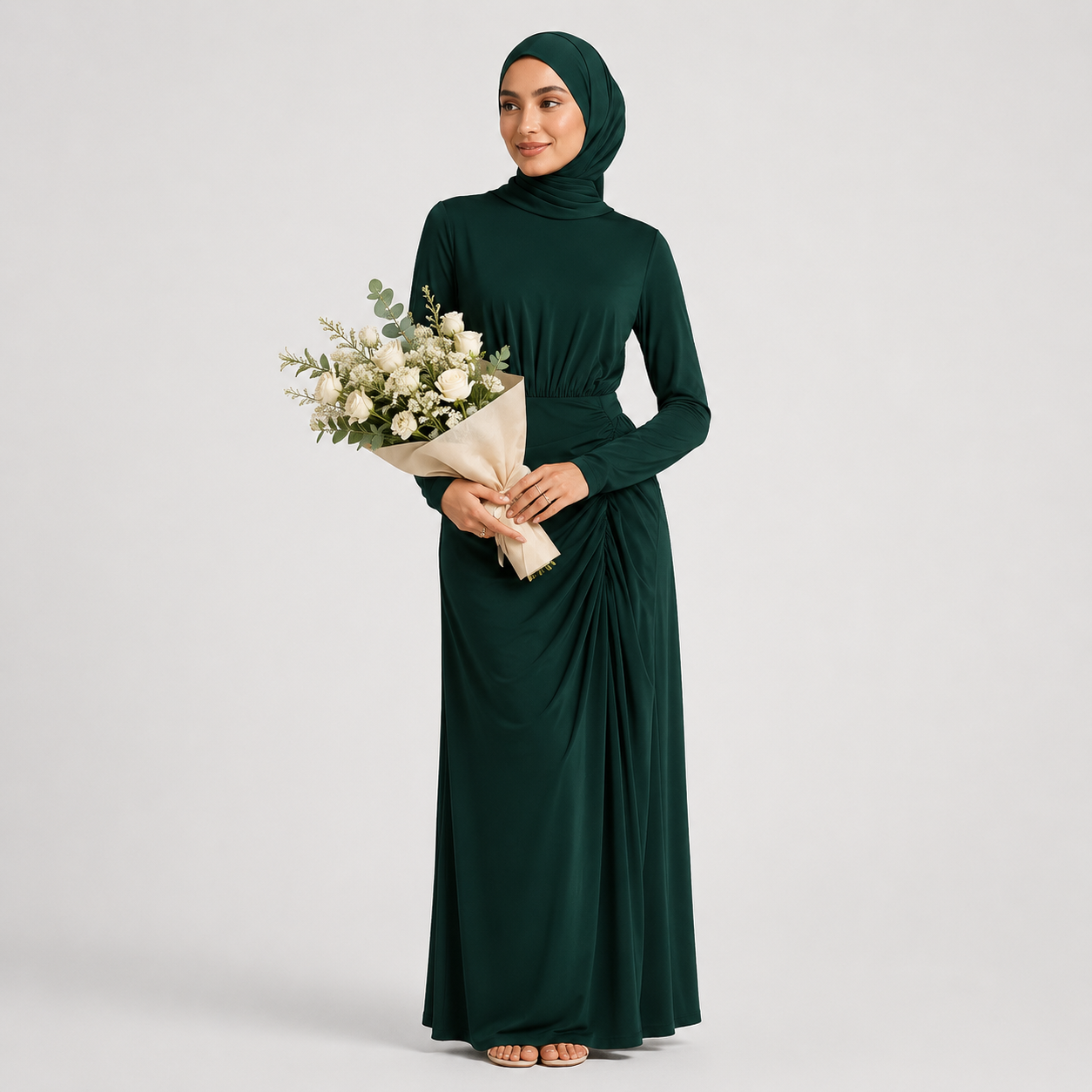 Woman in a long dark green dress holding a bouquet of flowers on a light gray background