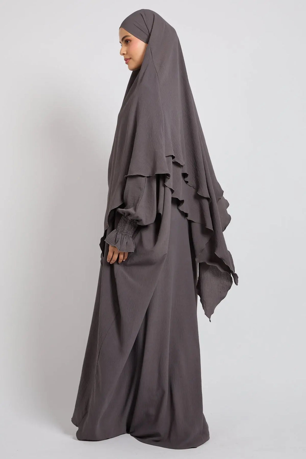 Woman wearing a gray abaya with ruffled sleeves on a white background
