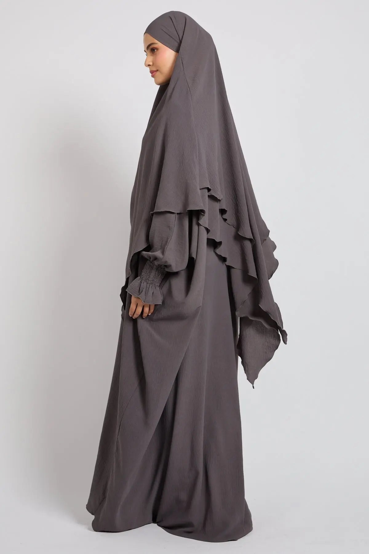 Woman wearing a gray abaya with ruffled sleeves on a white background