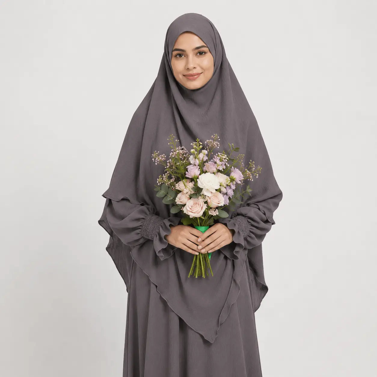 Woman wearing a gray hijab and dress holding a bouquet of flowers on a white background
