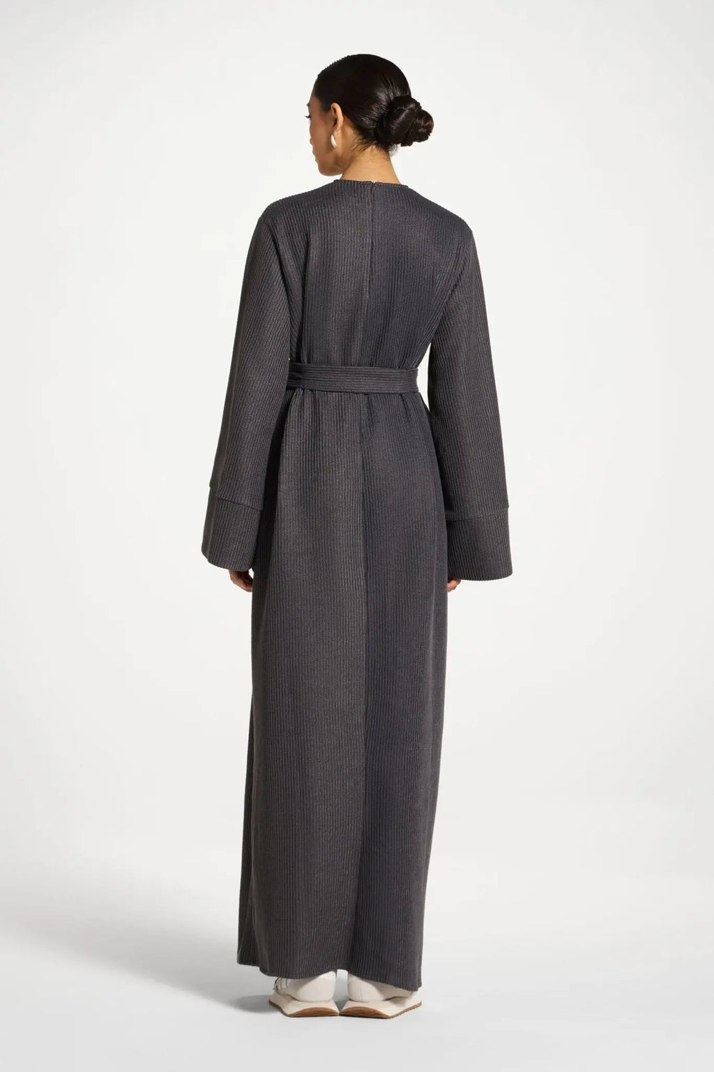 Person wearing a long gray dress with a belt on a white background