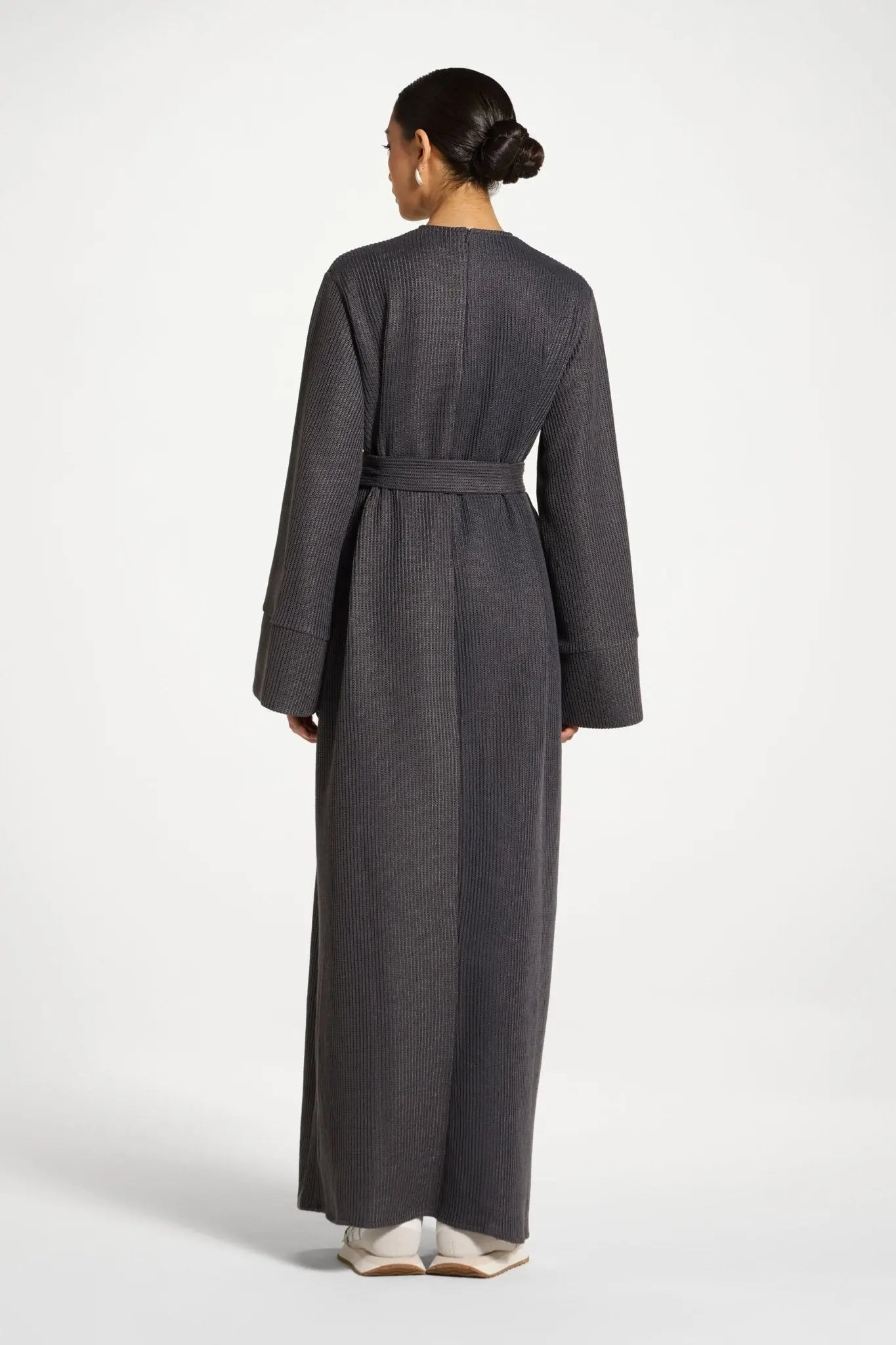 Person wearing a long gray dress with a belt on a white background