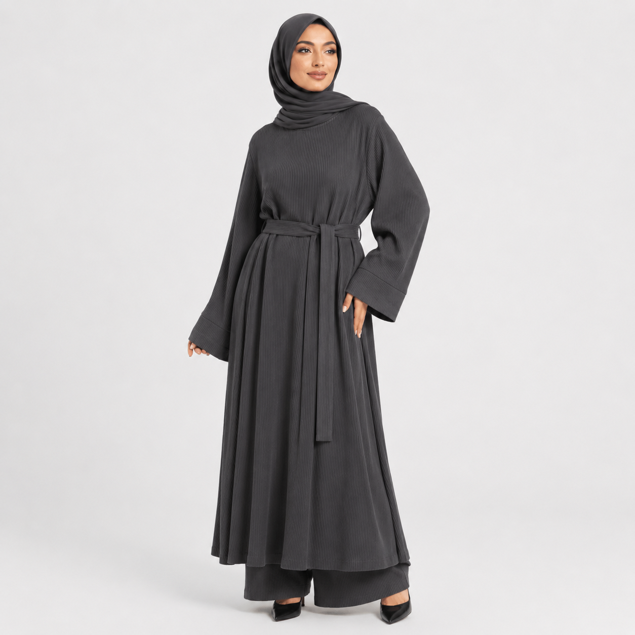 Woman wearing a dark gray abaya with a belt on a light gray background