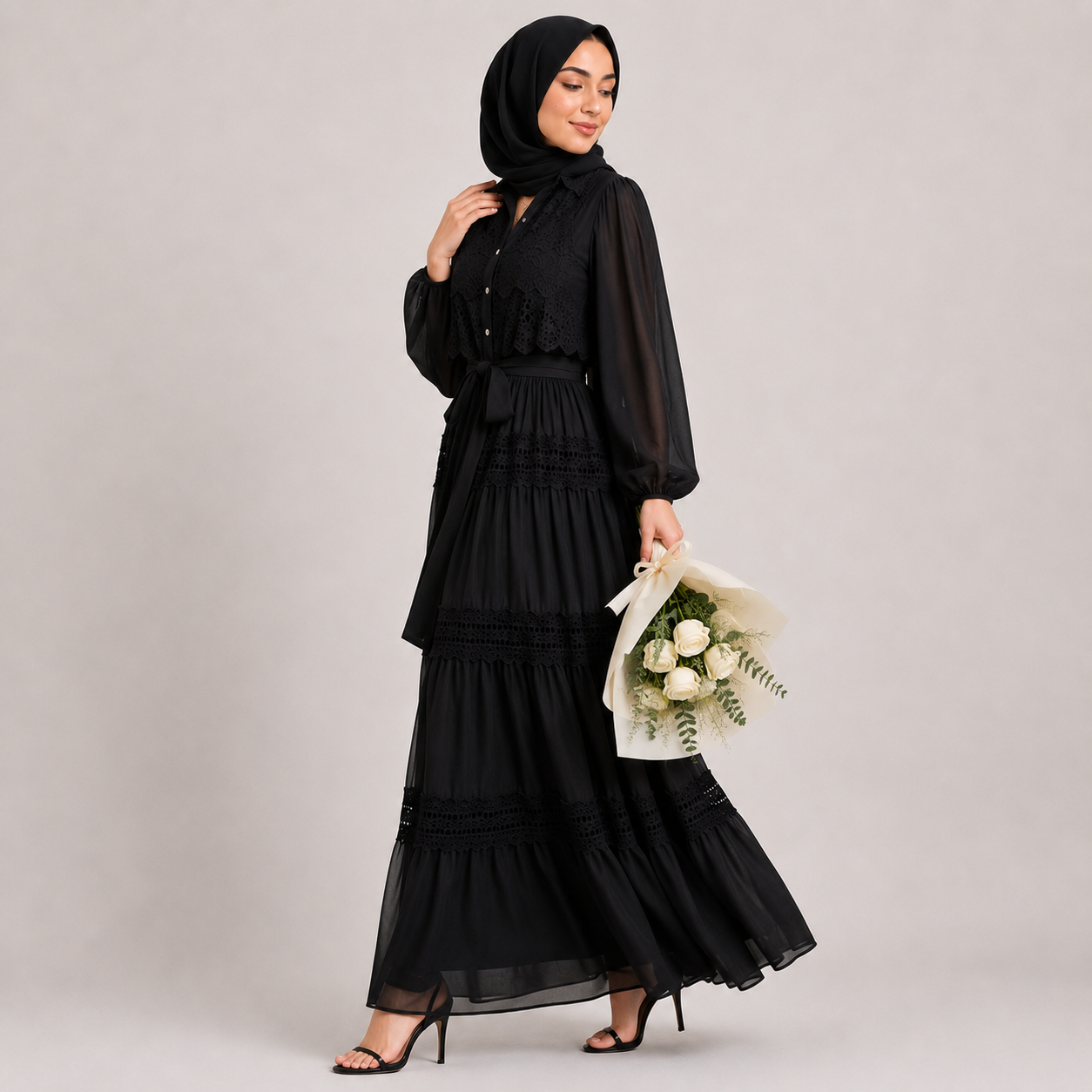 Woman in a black hijab and dress holding a bouquet of flowers on a plain background