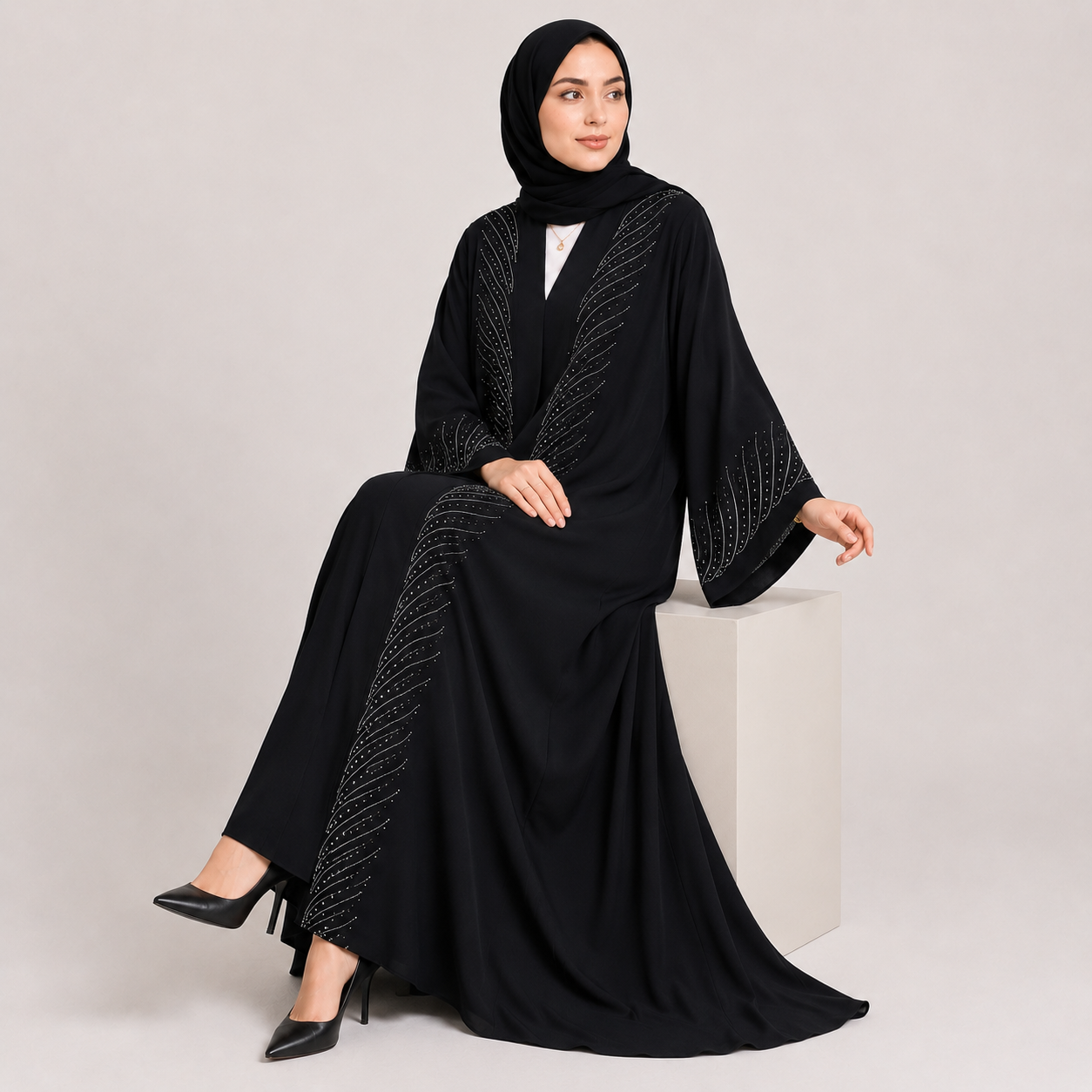 Woman wearing a black abaya with intricate designs on a light gray background