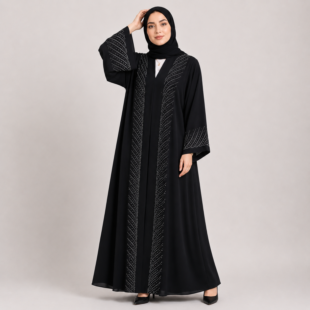 Woman wearing a black abaya with intricate designs on a plain background