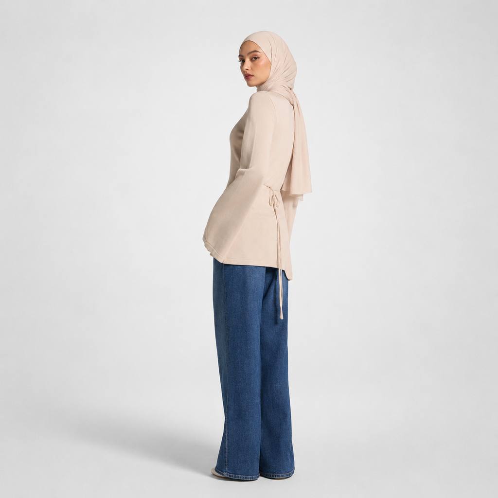 Woman wearing a beige hijab and blue jeans on a white background