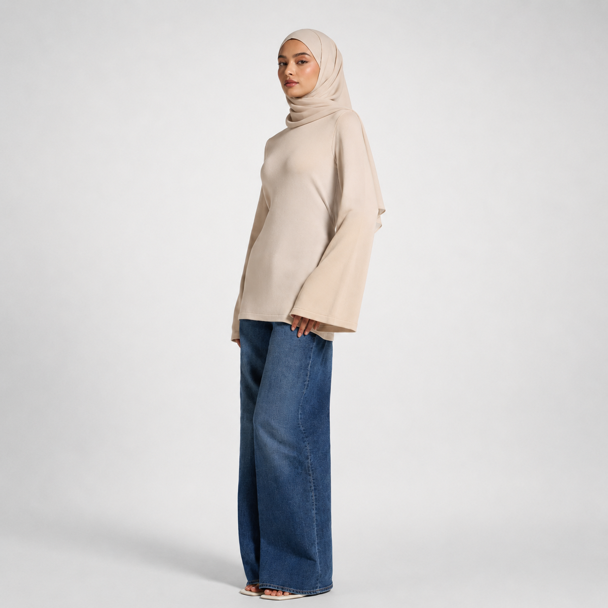 Woman wearing a beige hijab and blue jeans on a white background