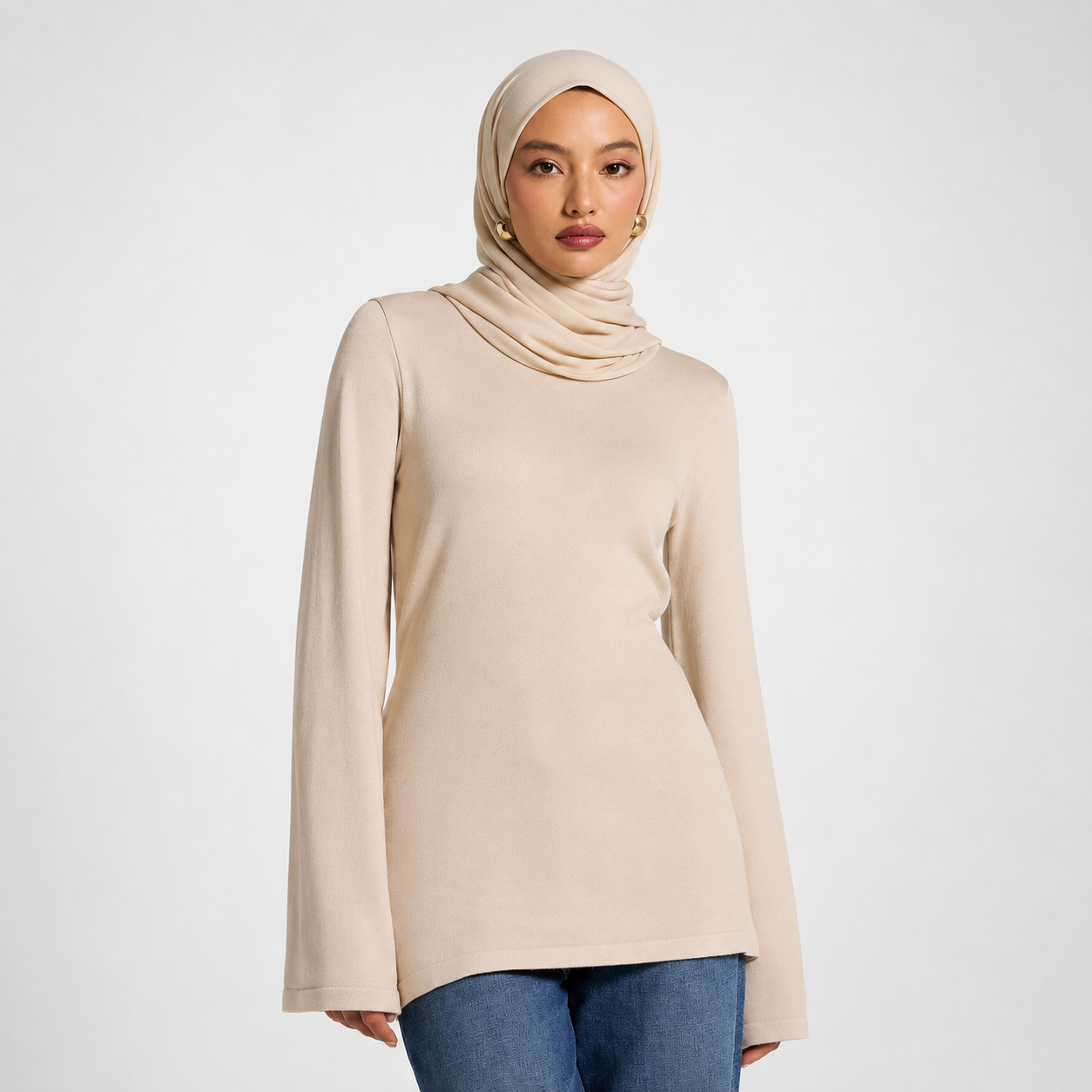 Woman wearing a beige hijab and long-sleeve top on a white background