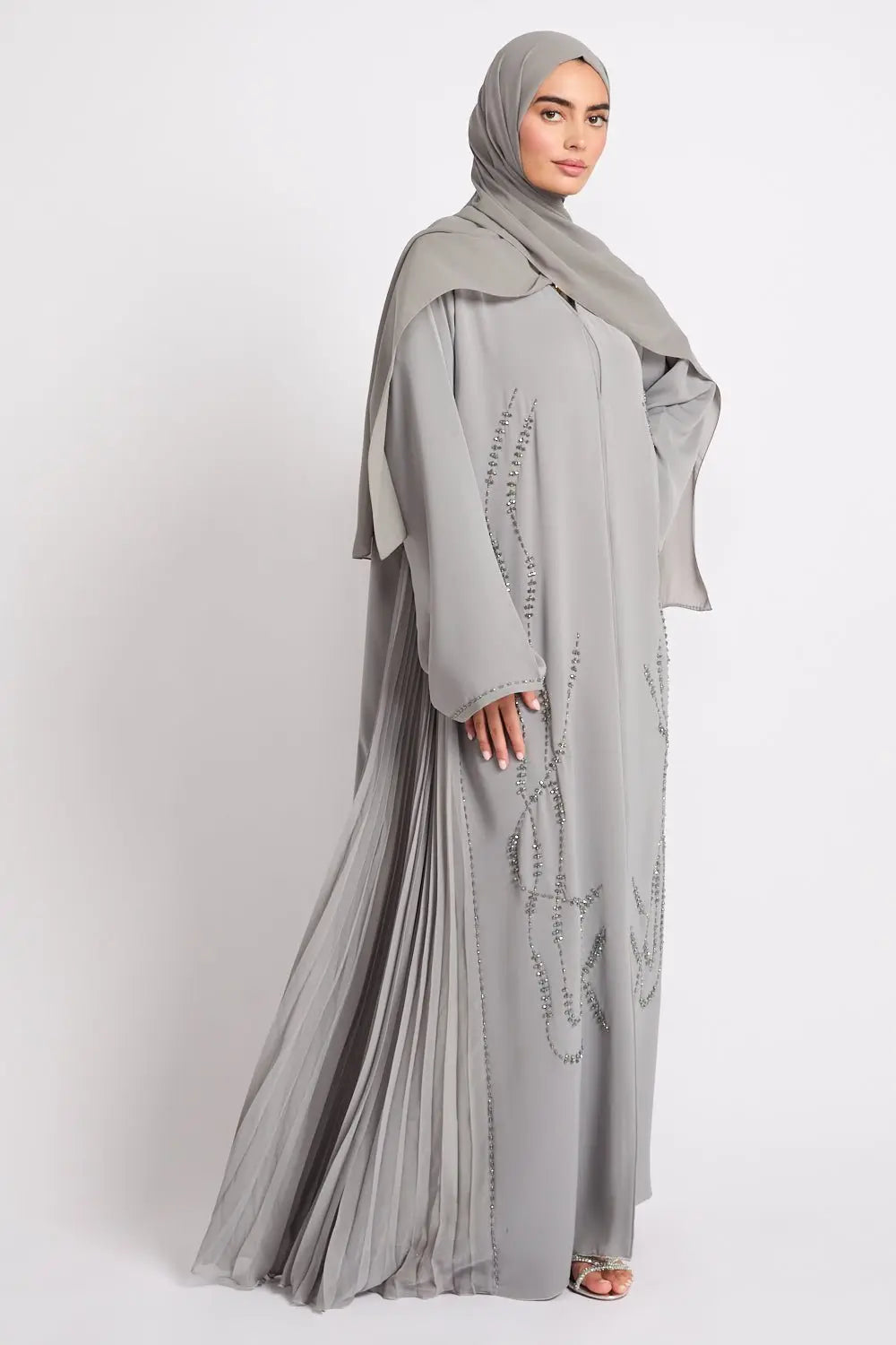 Woman wearing a gray abaya with intricate designs on a white background