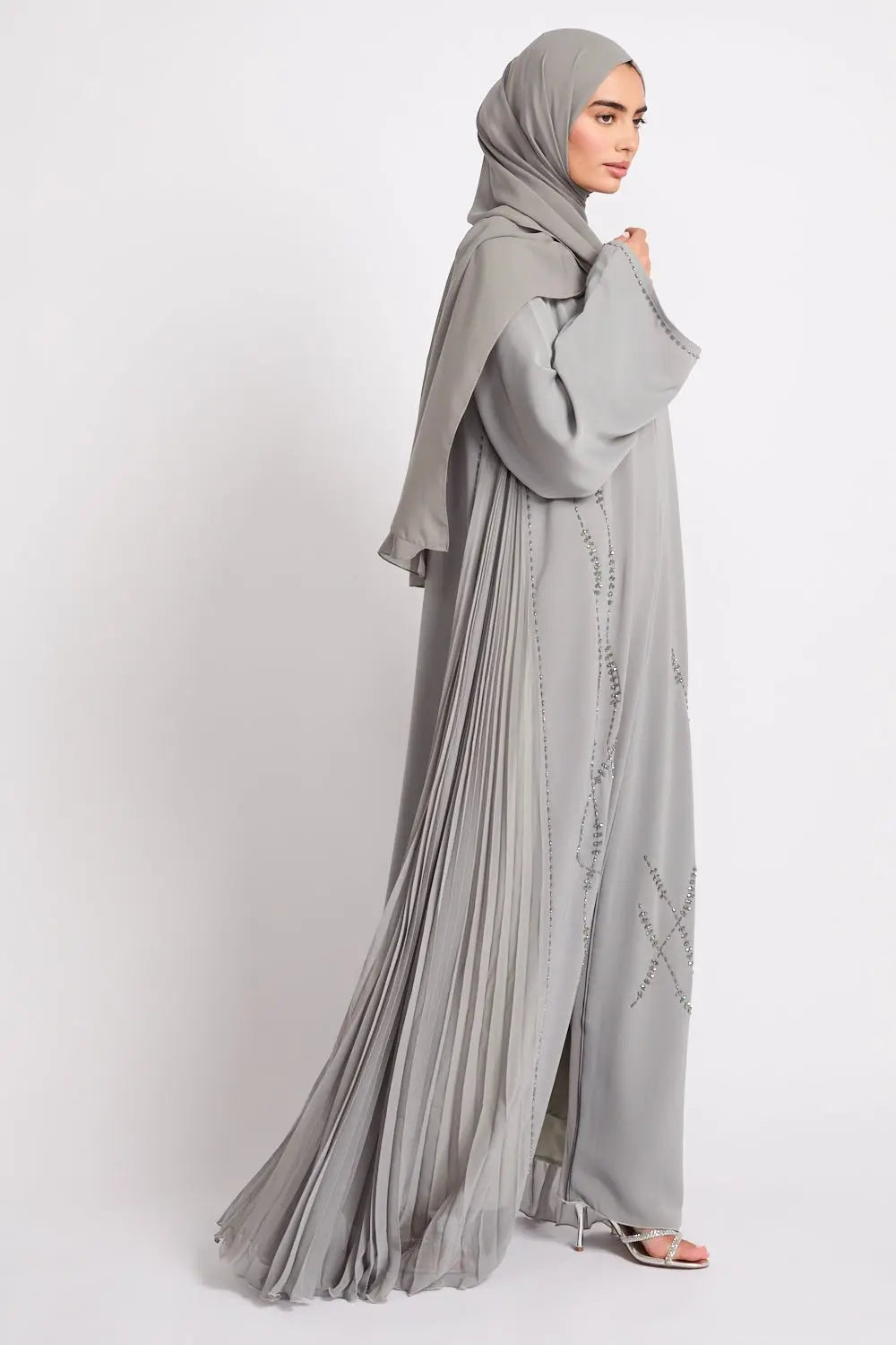 Woman wearing a long, light gray dress with a matching hijab on a white background