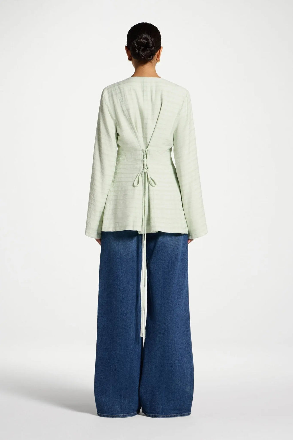 Person wearing a light green jacket and blue pants on a white background