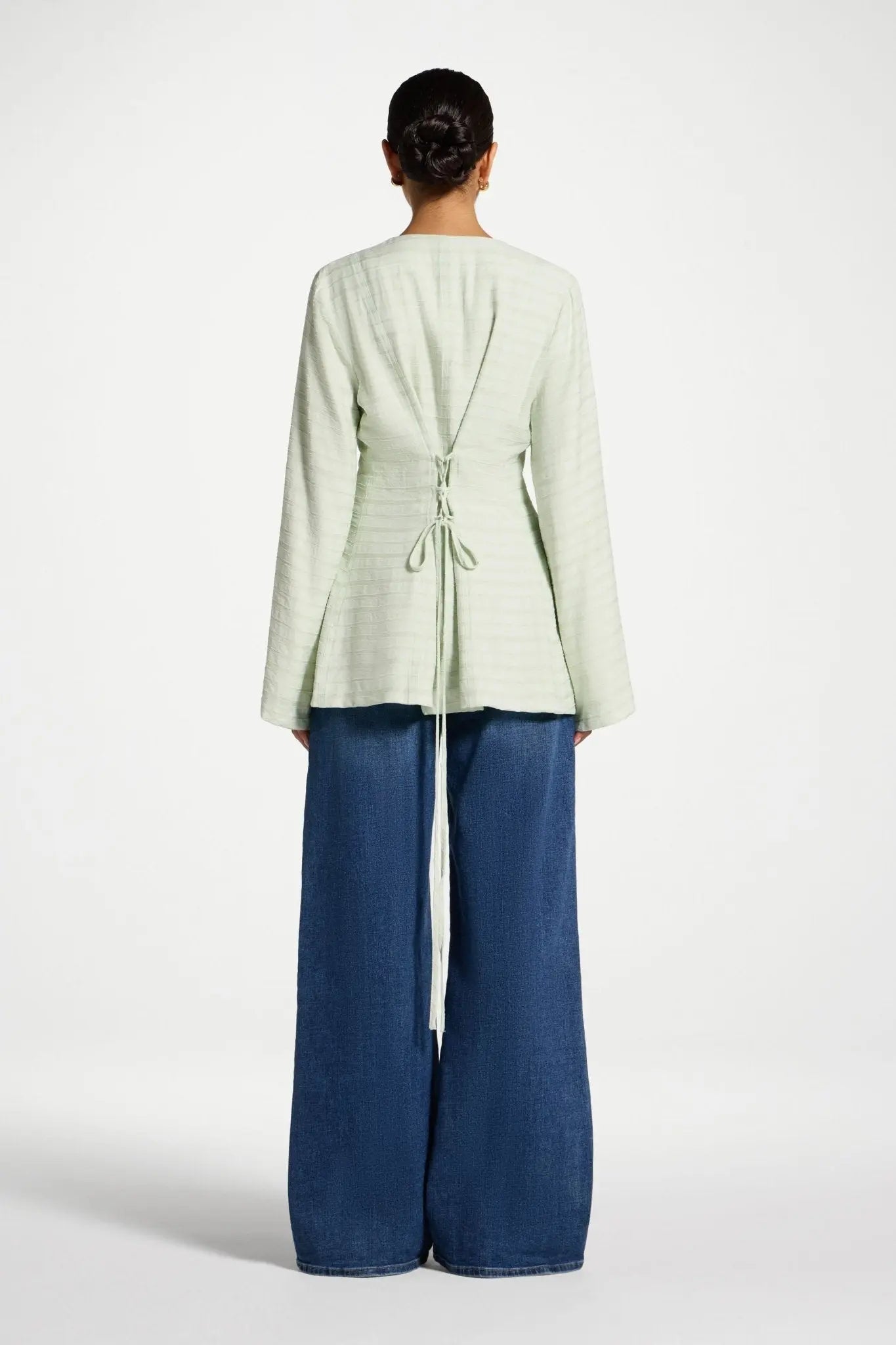 Person wearing a light green jacket and blue pants on a white background