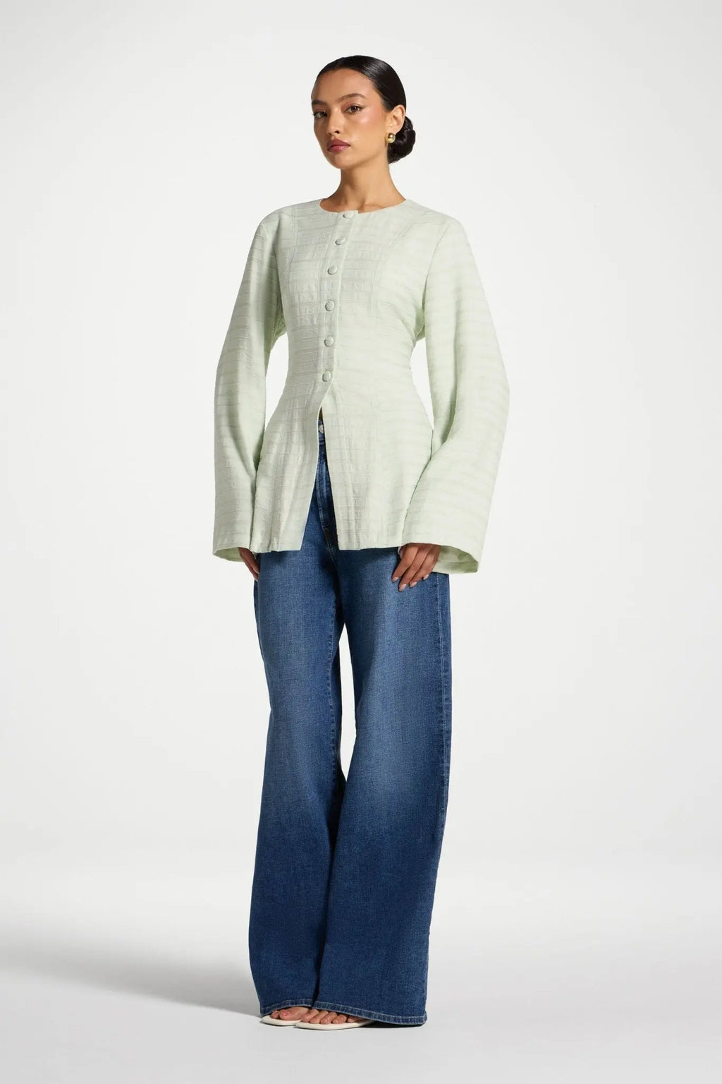 Woman wearing a light green cardigan and blue jeans on a white background