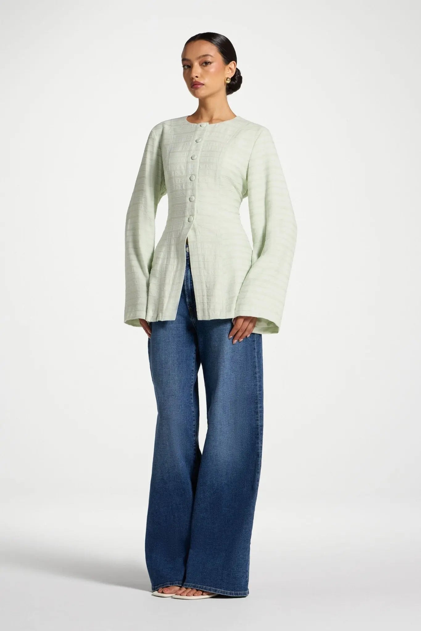 Woman wearing a light green cardigan and blue jeans on a white background
