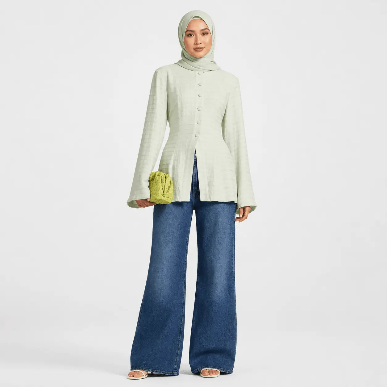 Woman wearing a light green cardigan and blue jeans on a white background
