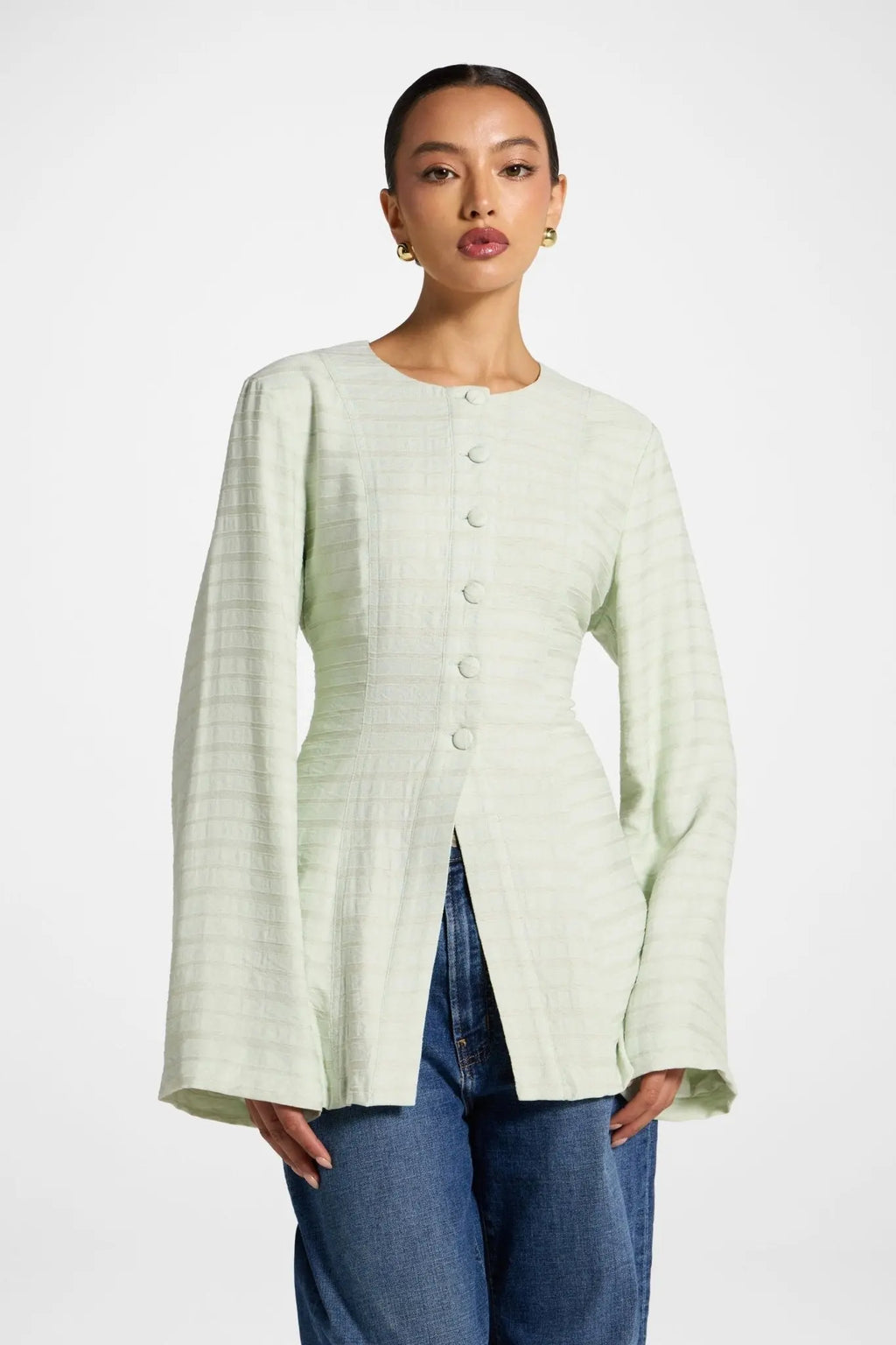 Woman wearing a light green textured cardigan over blue jeans on a white background
