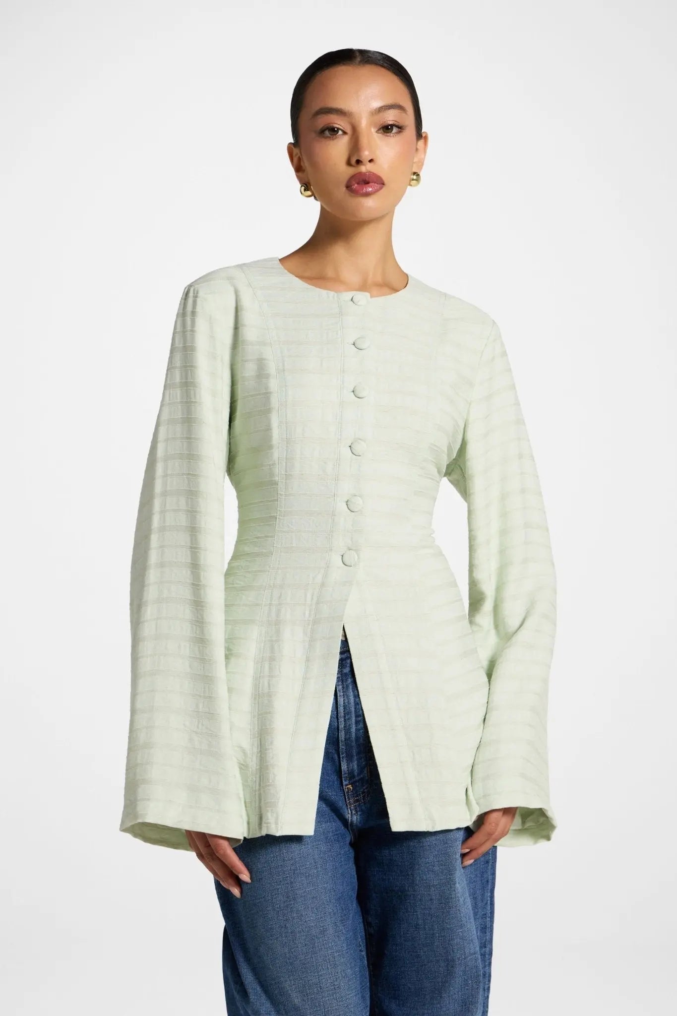 Woman wearing a light green textured cardigan over blue jeans on a white background