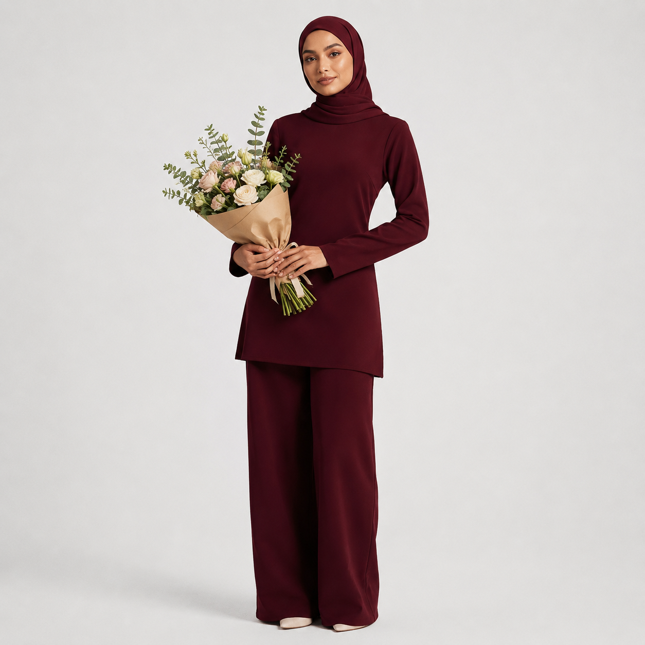 Woman in burgundy outfit holding a bouquet of flowers on a light gray background